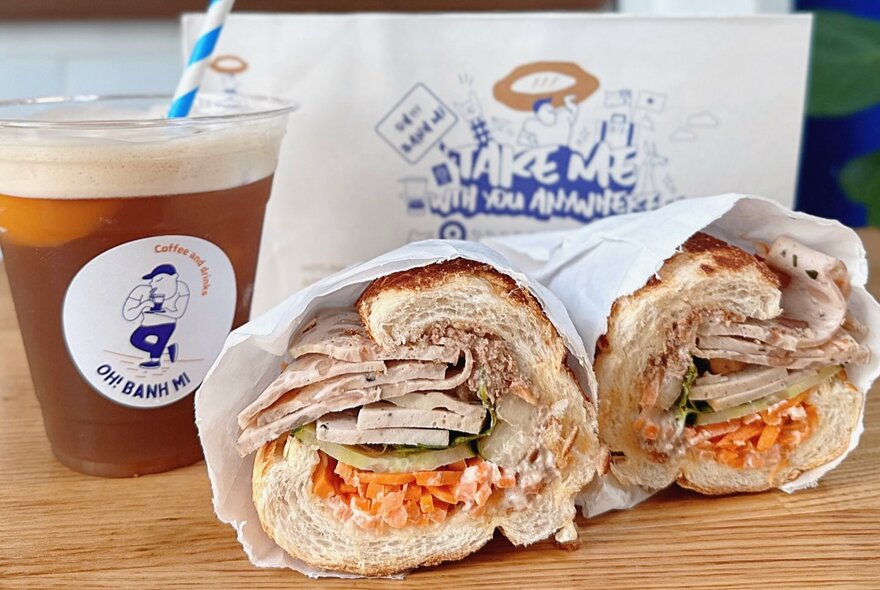 Sliced meat banh mi rolls next to a takeaway coffee with straw.