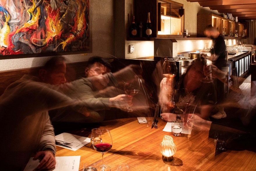 Dark dining setting with glasses of wine on a wooden table.