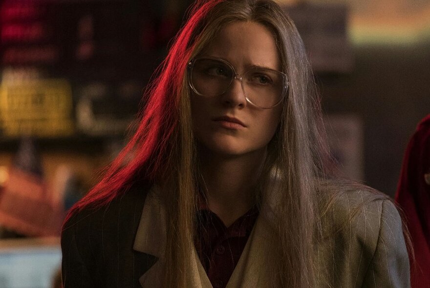 A  woman wearing glasses, with long straight hair framing her face, wearing a slightly oversized suit jacket.