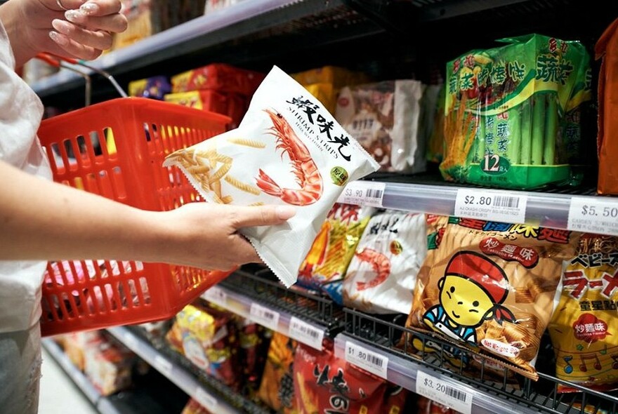 Interior of Tang Asian Food Emporium showing a shelf of products and someone shopping with a red basket. 