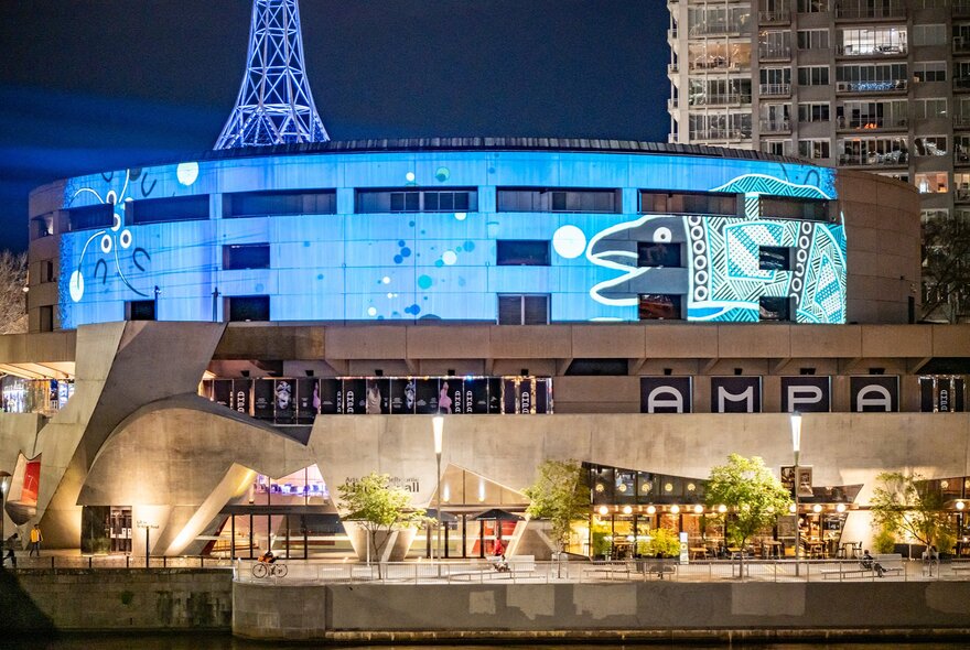 The Arts Centre illuminated at night with city buildings in the background.
