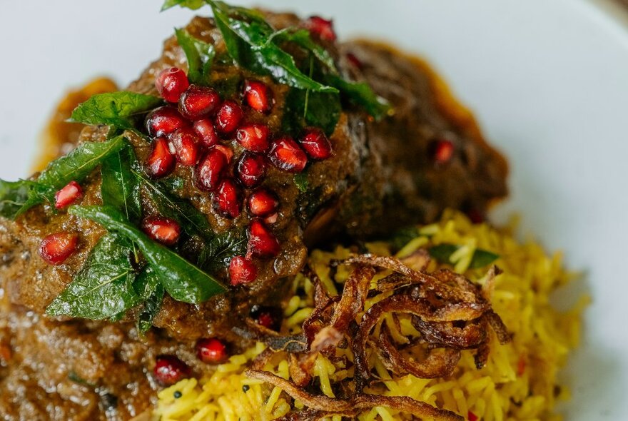 Close up of a meat dish served with saffron rice and a pomegranate garnish.