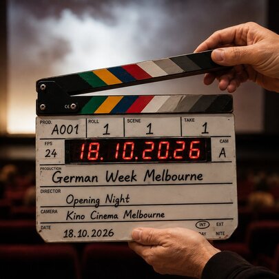 A film clapperboard being held up in front of a cinema screen from the back of the movie theatre.