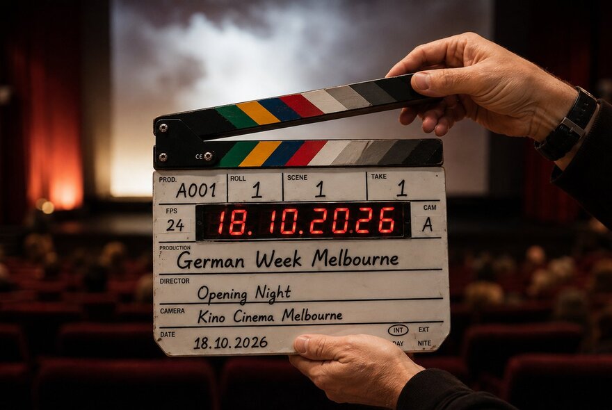 A film clapperboard being held up in front of a cinema screen from the back of the movie theatre.