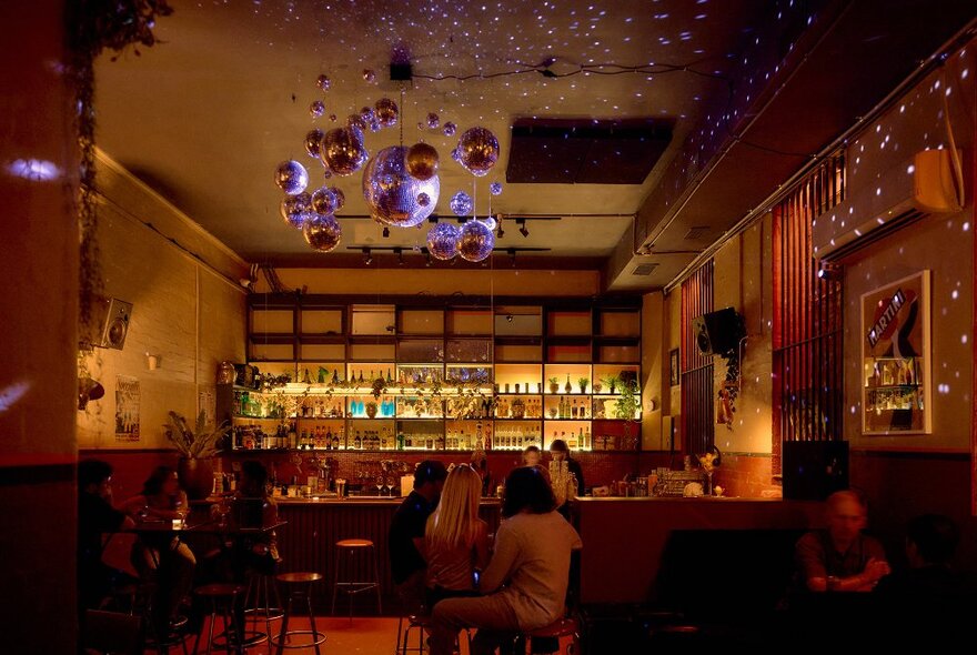 A busy bar with disco balls hanging from the ceiling. 