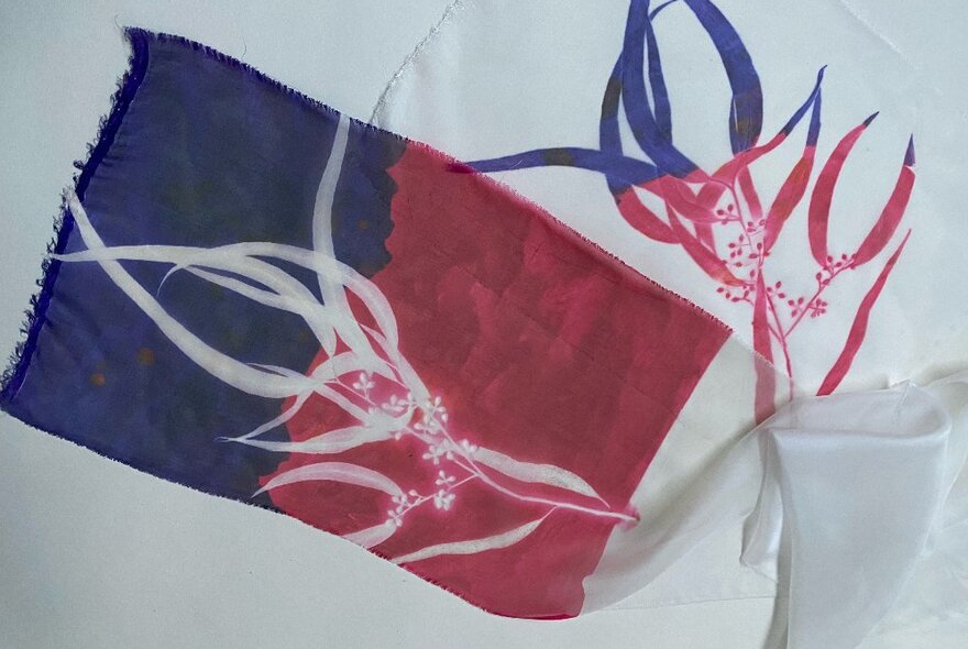 A hand printed scarf with a gum leaf pattern in red and blue on one half and in white on the other half.