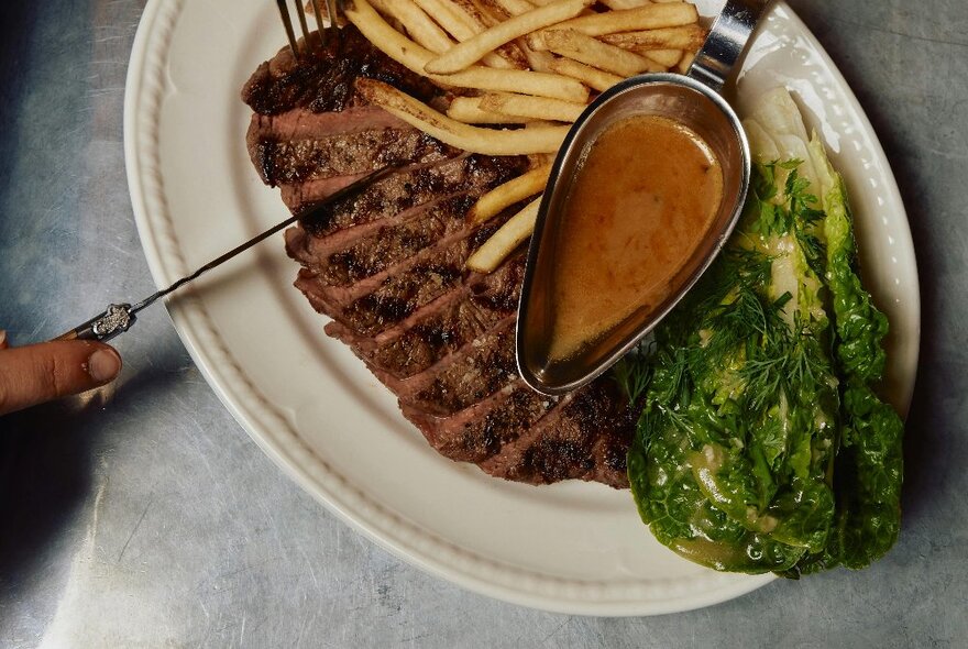 Steak, chips and salad on white oval plate with gravy boat.