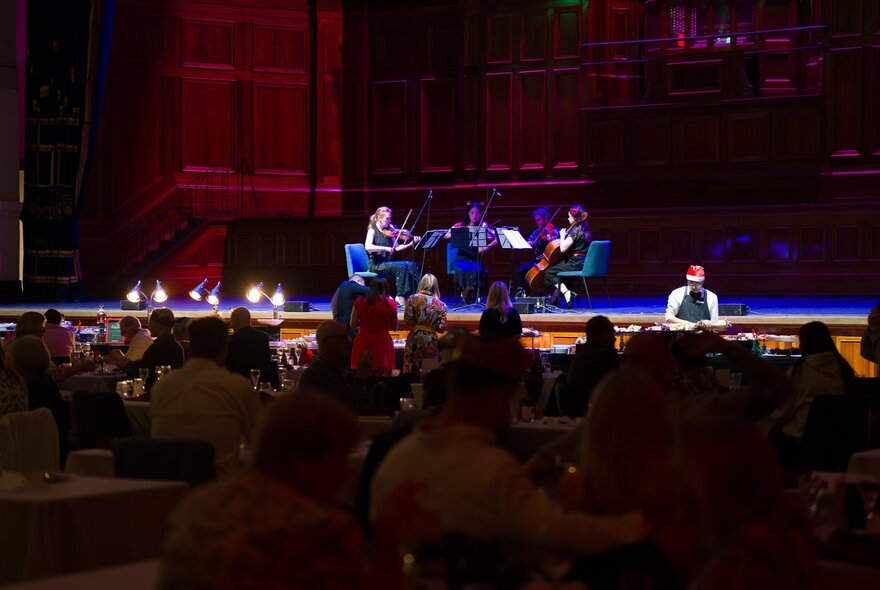 A string quarter on stage at Melbourne's Town Hall, with dining patrons watching on.