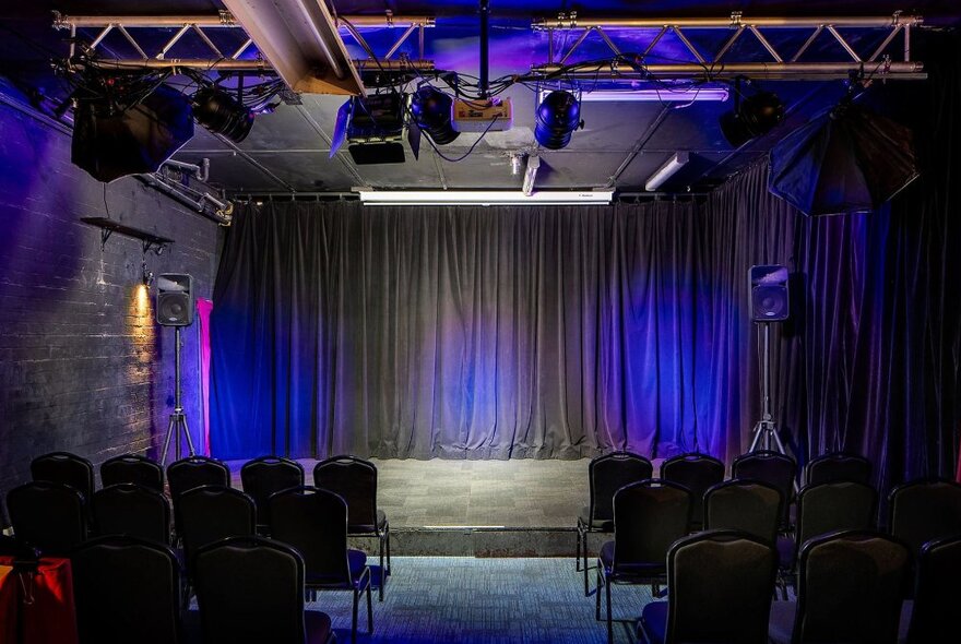 An empty stage with a black curtain, seen from behind the rows of empty chairs.