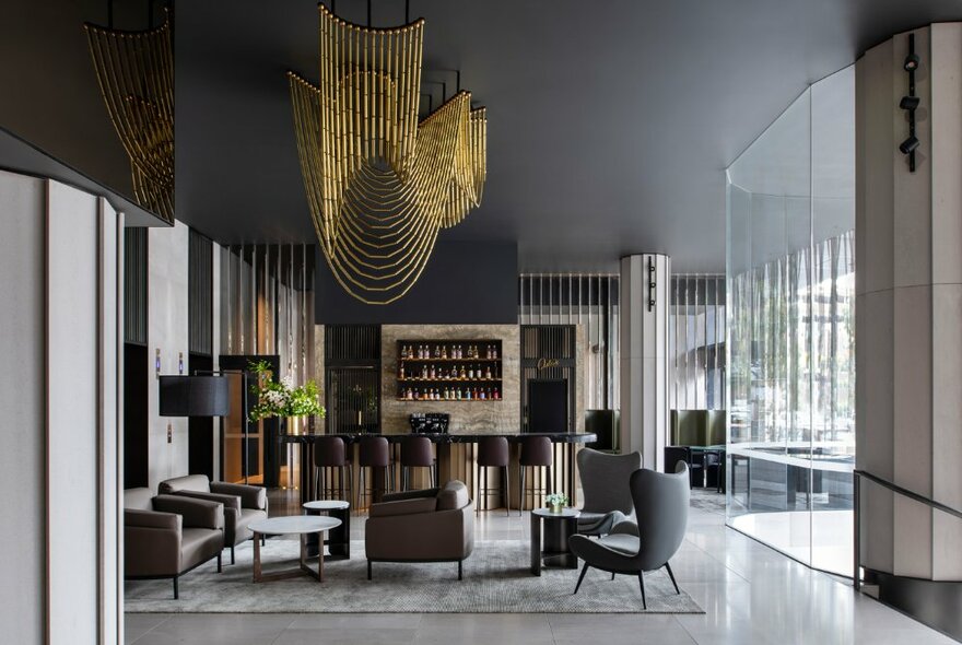 The lobby of the Melbourne Marriott Hotel with muted grey tones, timber accents and a striking gold chandelier.