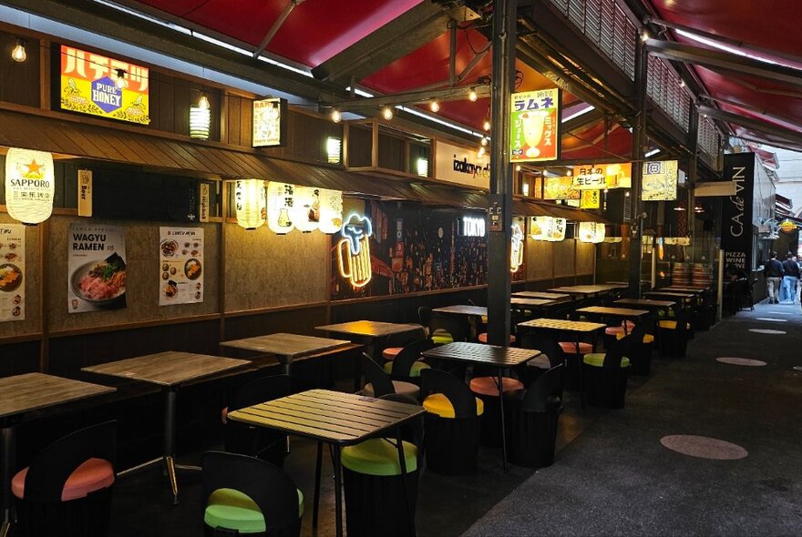 Japanese bar with lots of tables and chairs and illuminated signs for lighting.