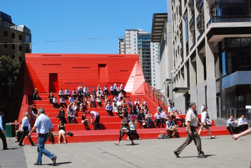 A gathering of people on red stars outdoors with other people walking past. 