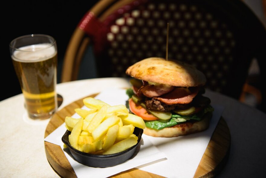 A table with a beer glass, a stacked hamburger and a small bowl of chips. 