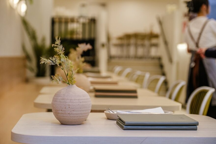 An empty cafe with tables for two and a pottery vases with small branches on the tables. 