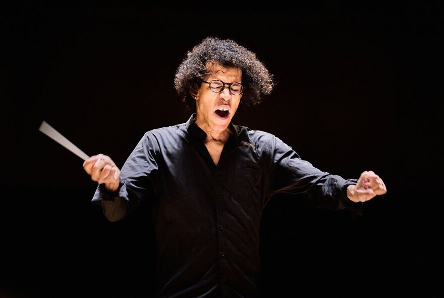 A conductor waving a baton with eyes closed and hands outstretched.