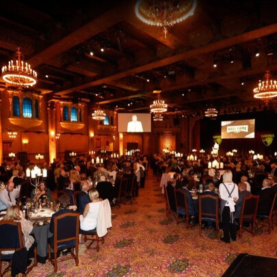 Diners seated at tables in chandelier-lit dining room with several large screens.