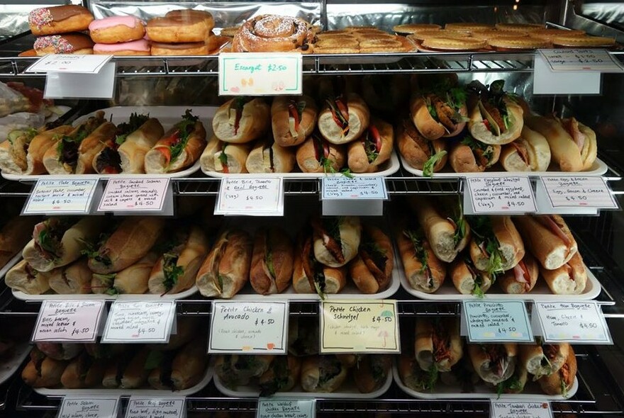 Counter with four shelves full of pastries and baguette sandwiches.