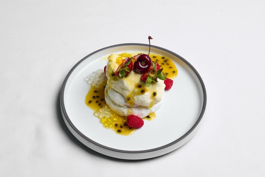 White plated dessert with fruit sauce and cherry.