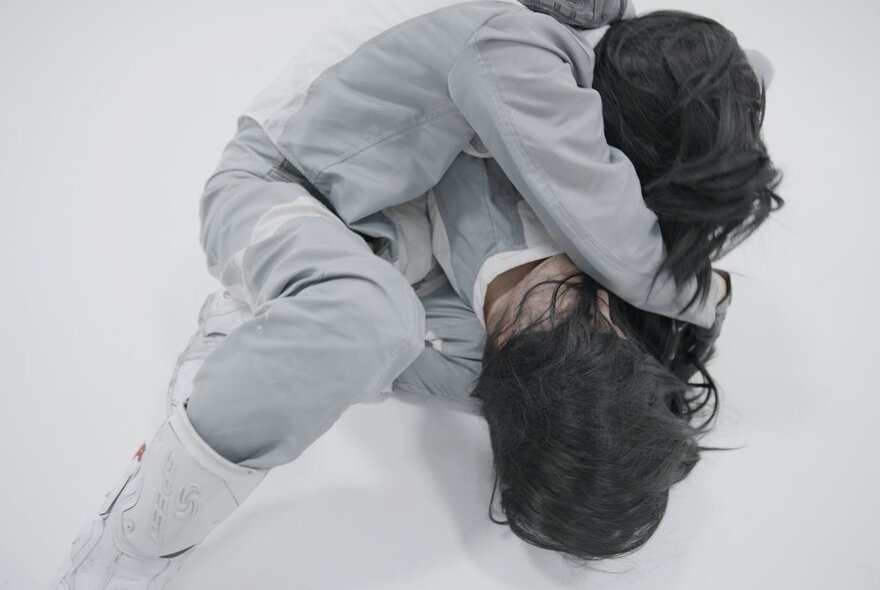 Two people, their faces not seen, wrestling in grey tracksuits. 