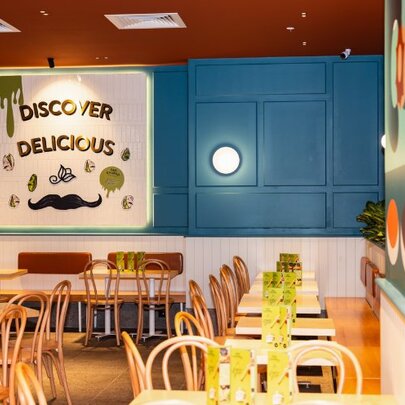 Interior of San Churro store at Southgate showing dining area with tables and chairs, blue wall and a sign on the back wall. 