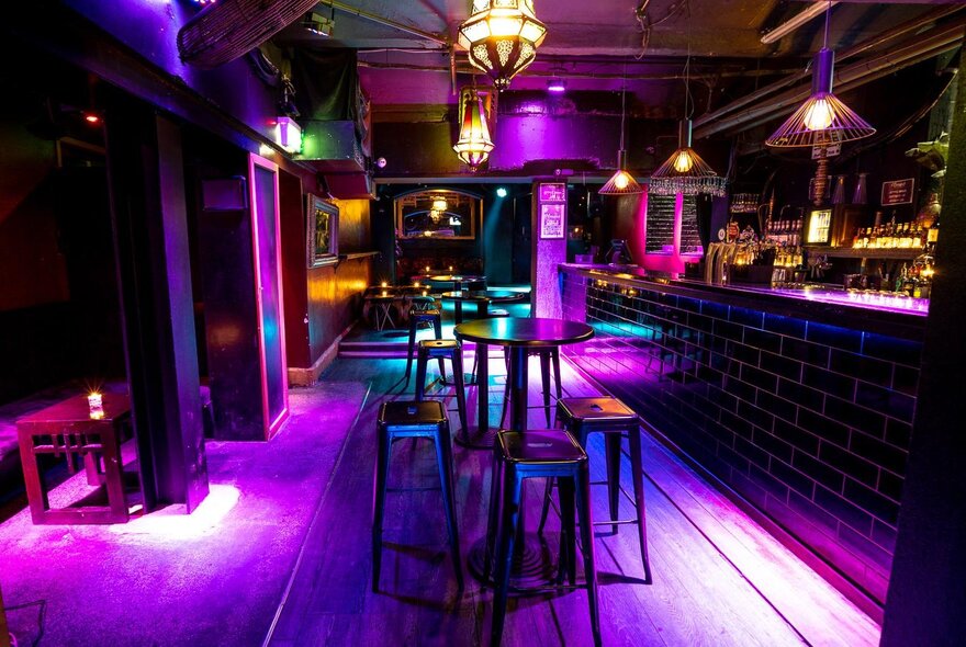 Purple-lit bar interior with bar seating and chandeliers.