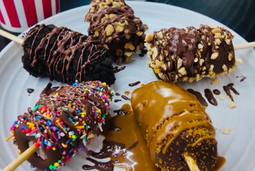 Five chocolate desserts on sticks, presented on a plate.