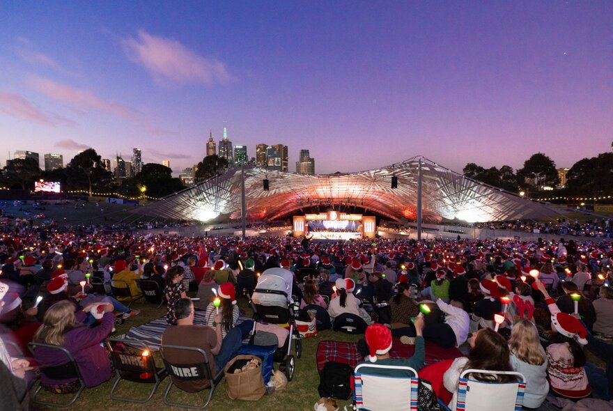 Audience seated before illuminated Sidney Myer Music Bowl stage at twilight.
