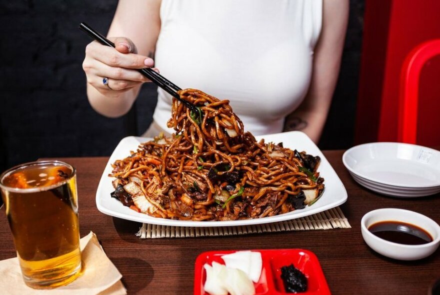 A woman in a white top lifting some noodles off a plate.