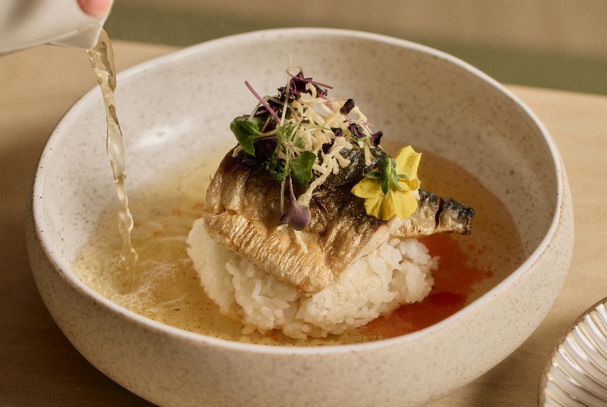 Hot broth being poured into a bowl of rice and fish.