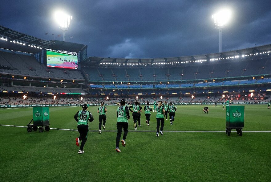 The Melbourne Stars WBBL team running out on to the grass at the MCG under lights.