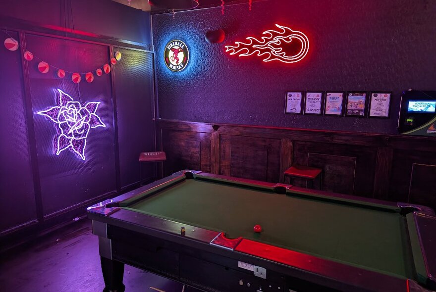 A dark bar room with a pool table and neon lights on the walls. 