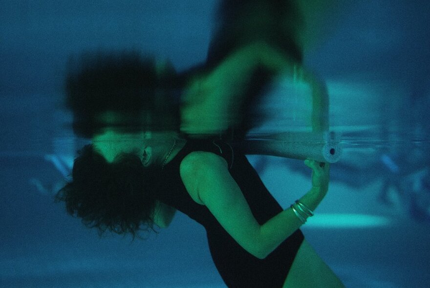 A woman underwater wearing a black bathing suit, listening to underwater music.