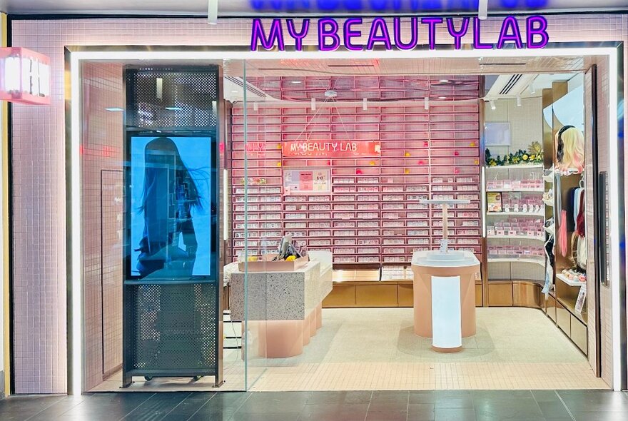 Shopping mall store with purple signage, pink wall lined with fingernail storage shelves, video screen and counters.