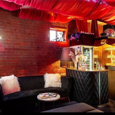 The cosy, intimate bar and lobby area of Club Voltaire with a black couch, soft lighting and billowing red fabric suspended across the ceiling.