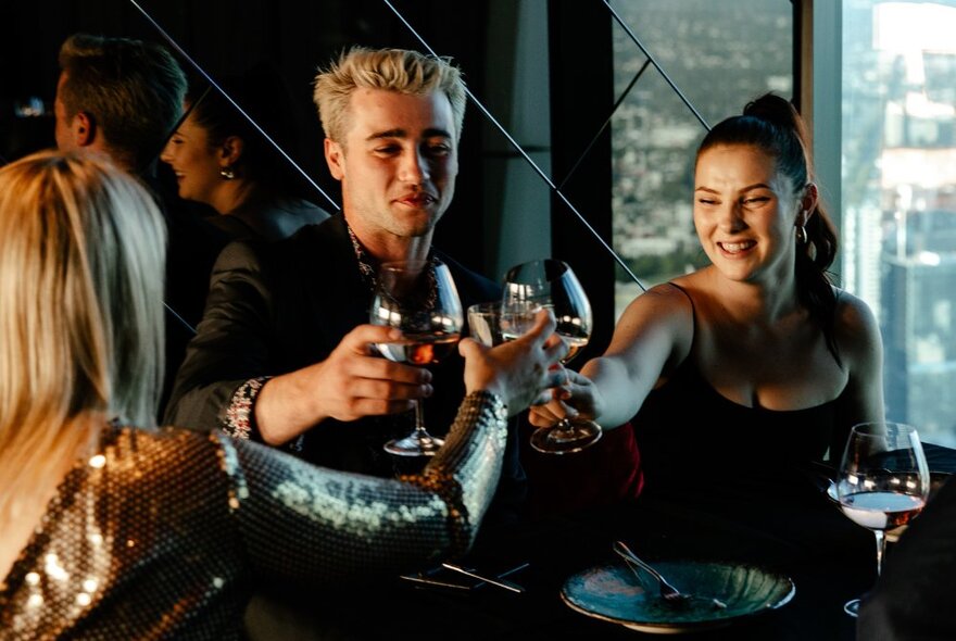 Three friends socialising and clinking their drinks in glasses at a bar.