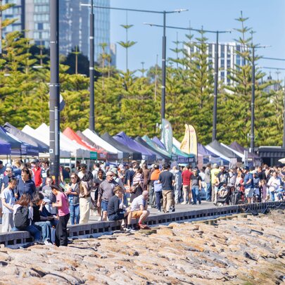 A crowd of people at a waterfront market with rows of marquee umbrellas.