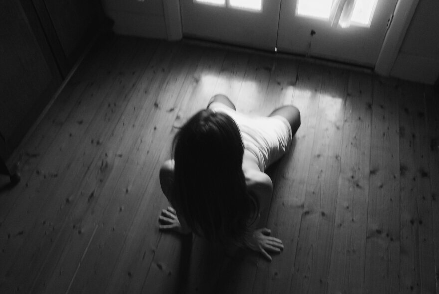 A woman squatting on a wooden floor, balancing her raised torso on her arms.