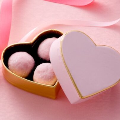 A pink, heart-shaped box lying open with three pink truffles inside.