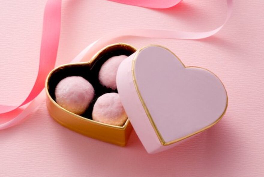 A pink, heart-shaped box lying open with three pink truffles inside.