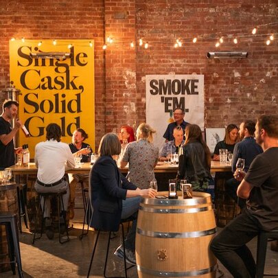 People seated in a distillery with brick walls, casks and tasting tables.