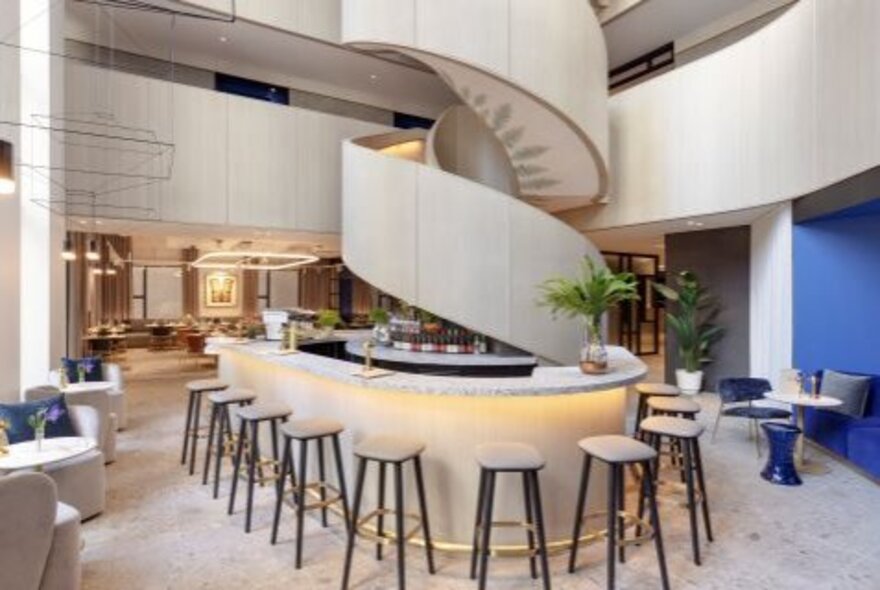 The modern interior of a bar in a hotel lobby, featuring a bold spiral staircase.