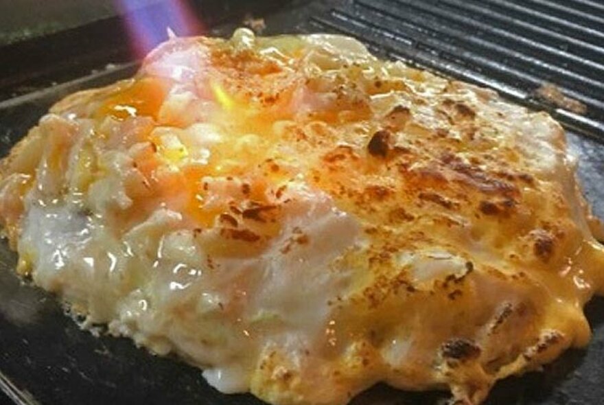 Japanese food on a grill with blow torch applied to brown the top.