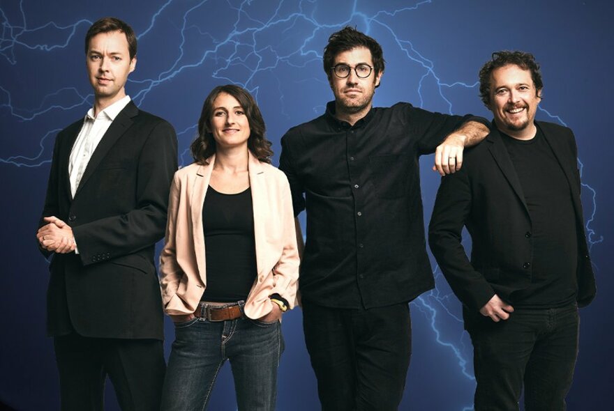 Three men and one woman, lined up in casual clothes against a blue background, all smiling and looking directly at the viewer.