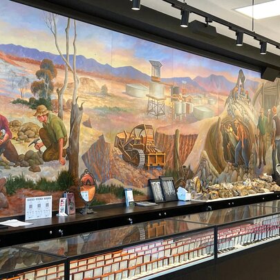 Interior of a jewellery store with long glass cabinets and a mural showing prospectors mining for opals