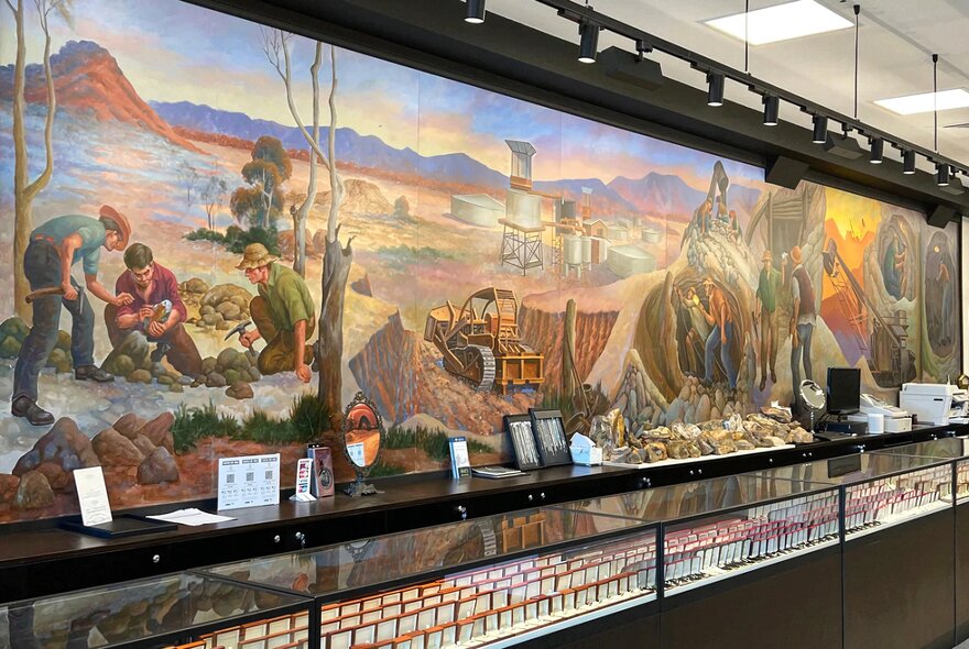 Interior of a jewellery store with long glass cabinets and a mural showing prospectors mining for opals