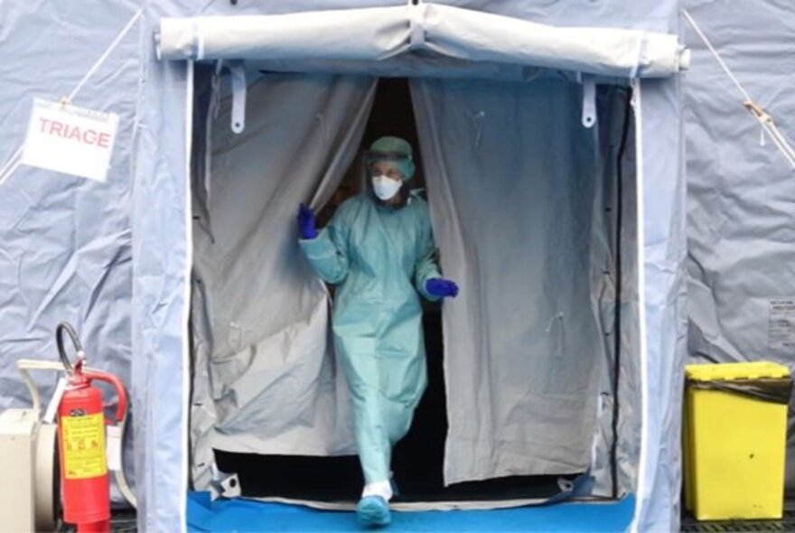 Pandemic-era worker wearing full suit, mask and gloves, emerging from secure tent flap.