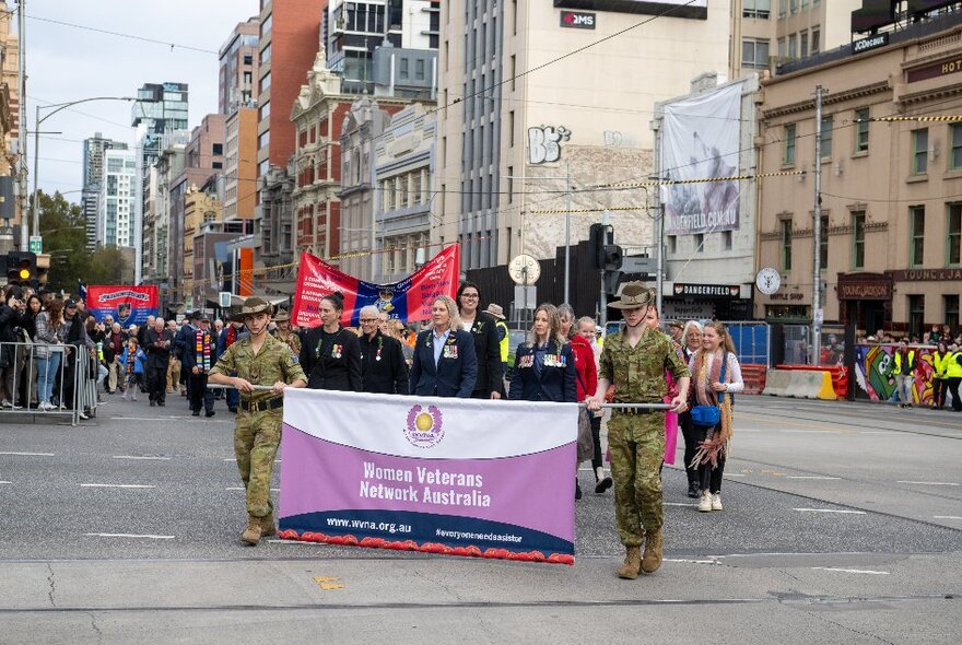 People participating in the ANZAC Day march through Melbourne, some holding banners and in military uniform. 