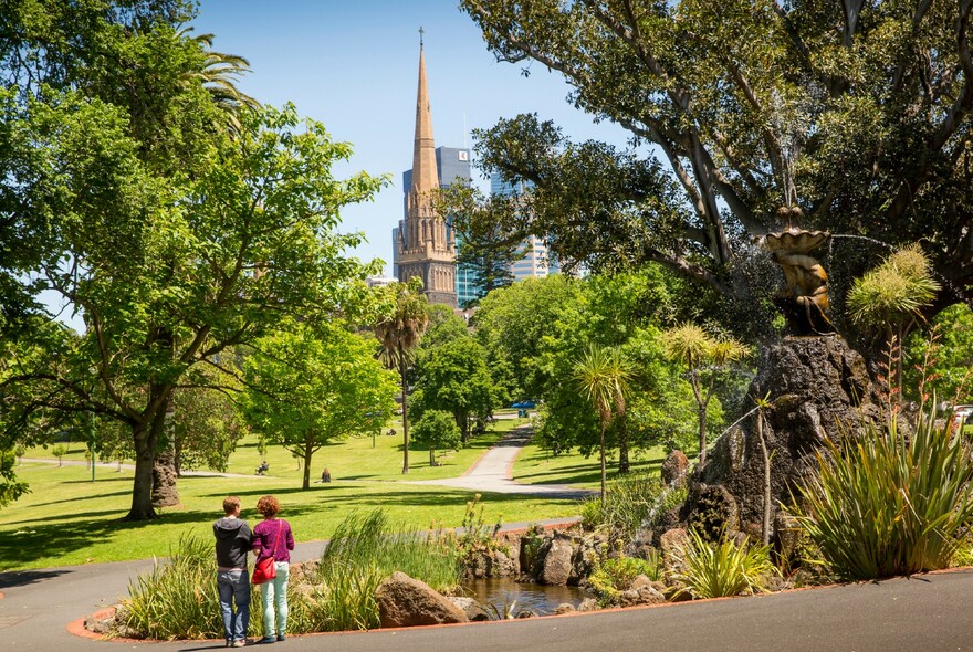 Visitors surveying the tranquil scene of Fitzroy Gardens fountain, lawns and trees,