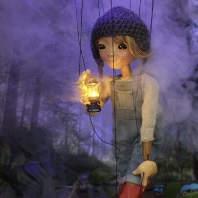 Puppet scene with a figure holding a lamp in a purple forest setting.