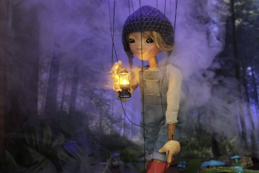 Puppet scene with a figure holding a lamp in a purple forest setting.
